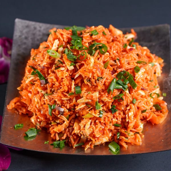 Close-up of a vibrant orange rice dish with shredded chicken and green onions on a dark plate.
